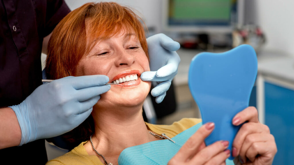 Photo of woman looking at teeth in mirror in dentist chair